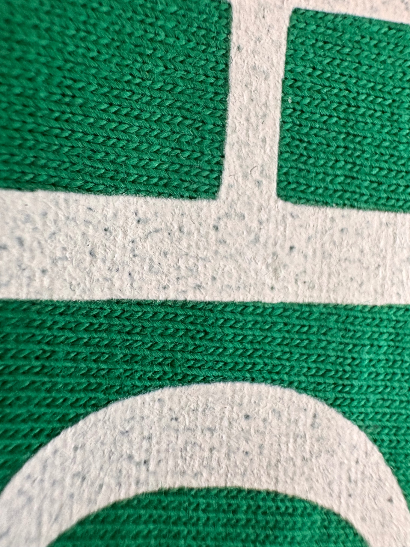 Macro photograph of white print on a green garment showing fine openings across the solid areas